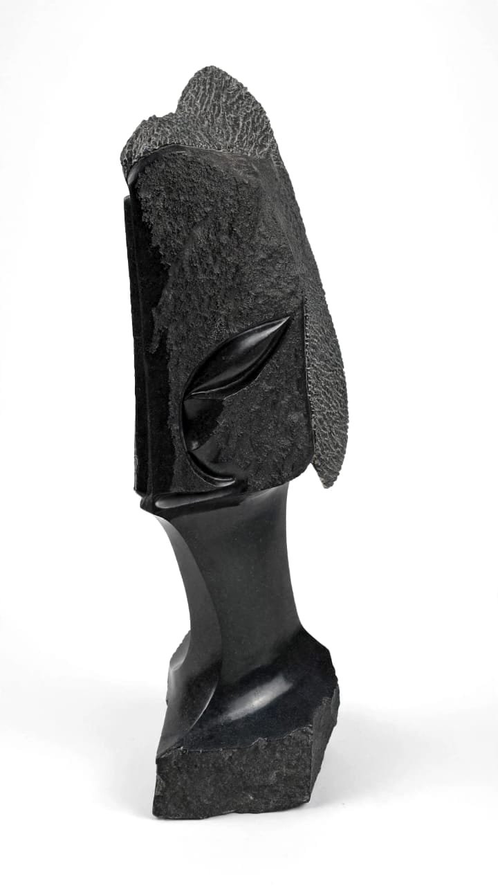 Dark stone head with a rough-textured crown and a carved leaf-shaped eye, on white