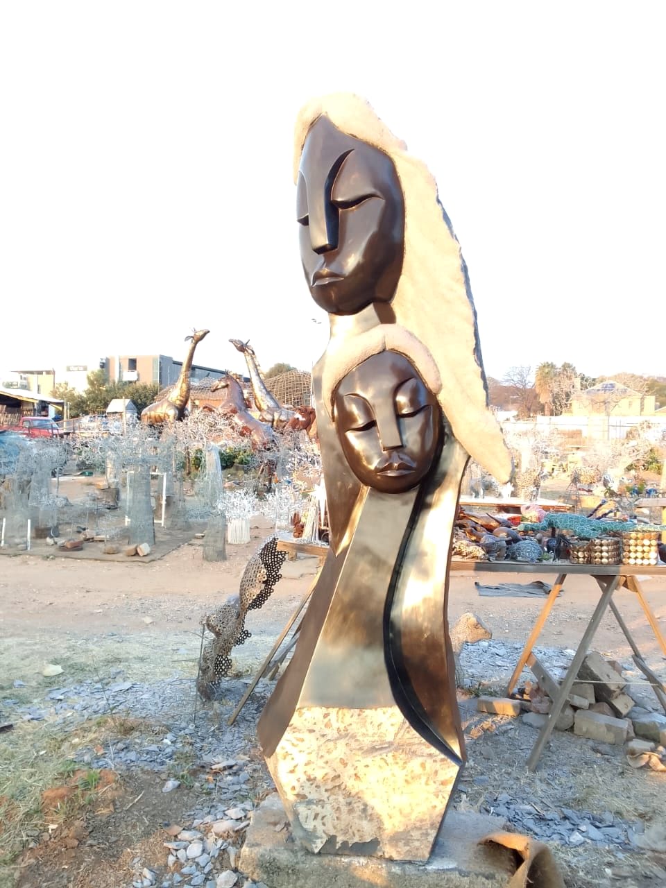 Finished stone sculpture of two faces, one above the other, polished to a dark gloss and framed by rough golden stone