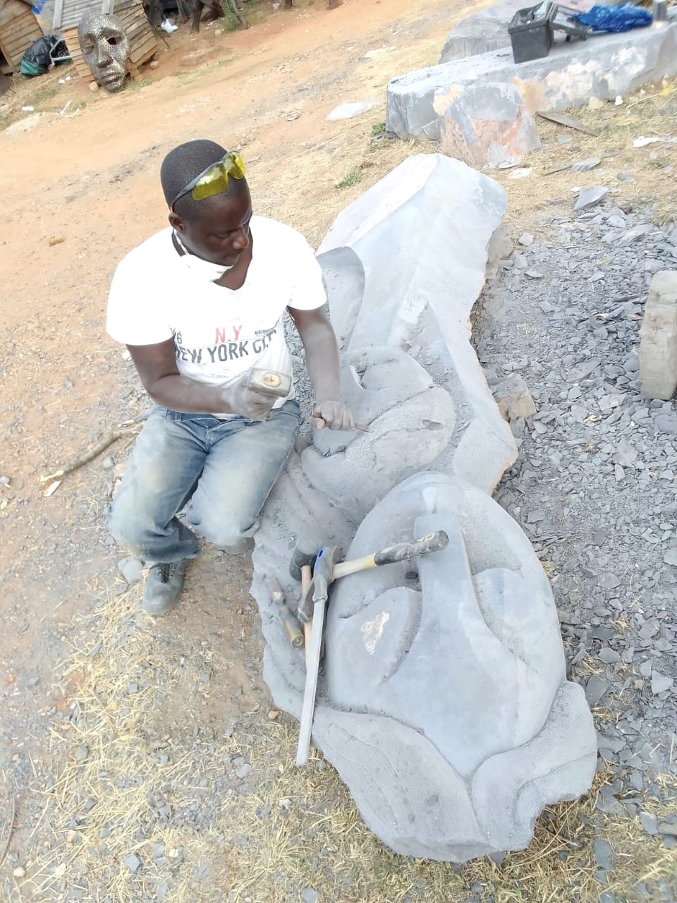 A carver in a white T-shirt and safety glasses working on the stone with hand tools