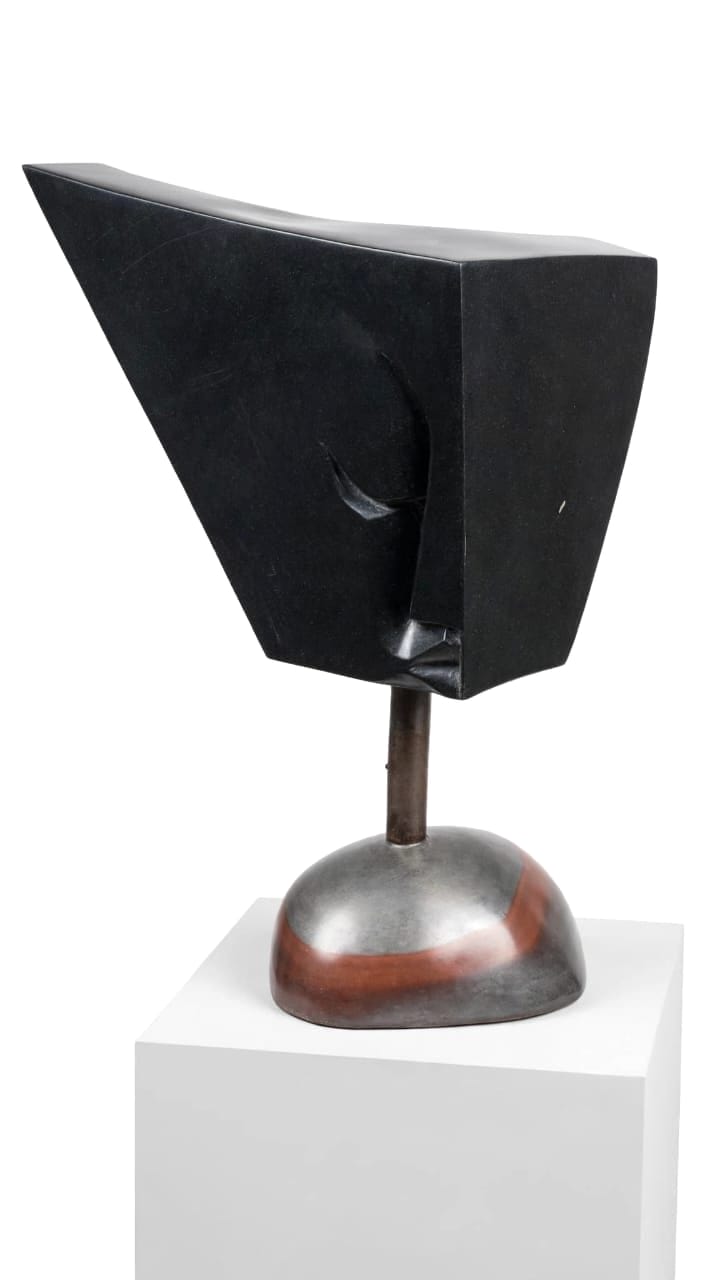 Angular black stone slab head on a steel rod and a steel and copper base, on a white pedestal
