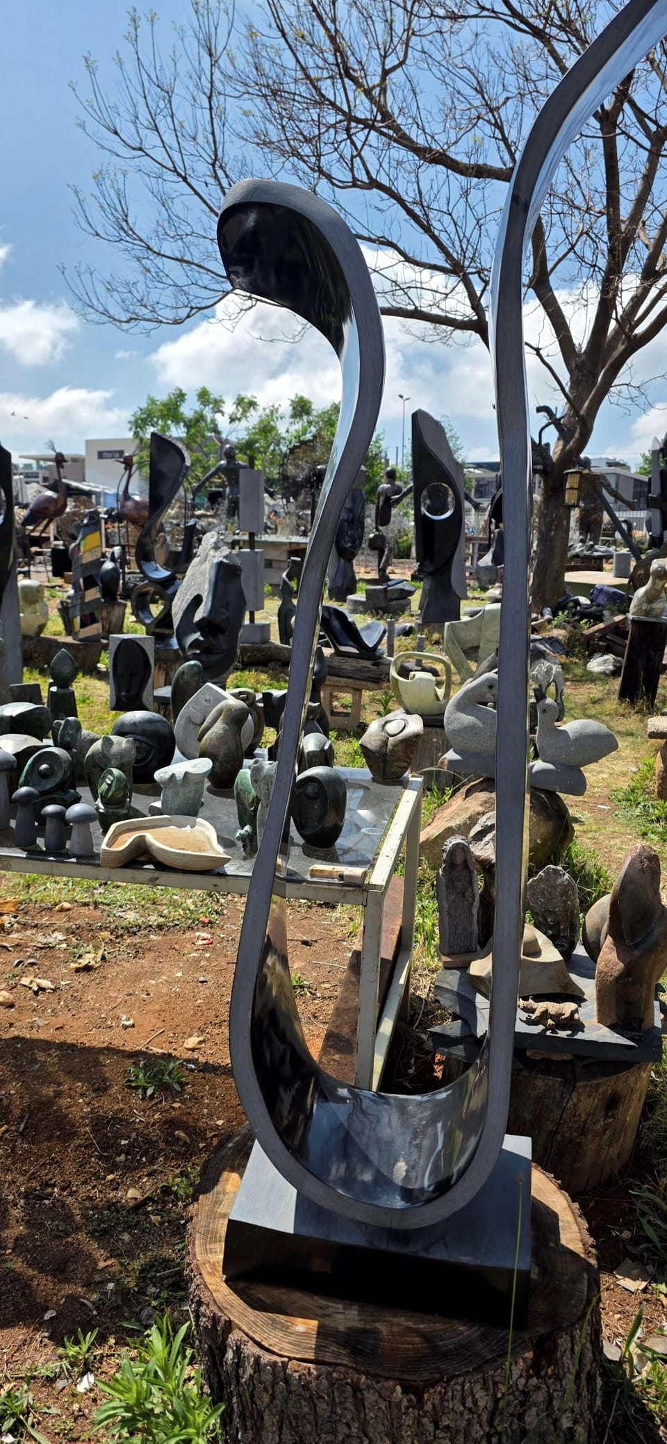 Open ribbon of polished dark stone curving up from a square base, with the workshop yard behind