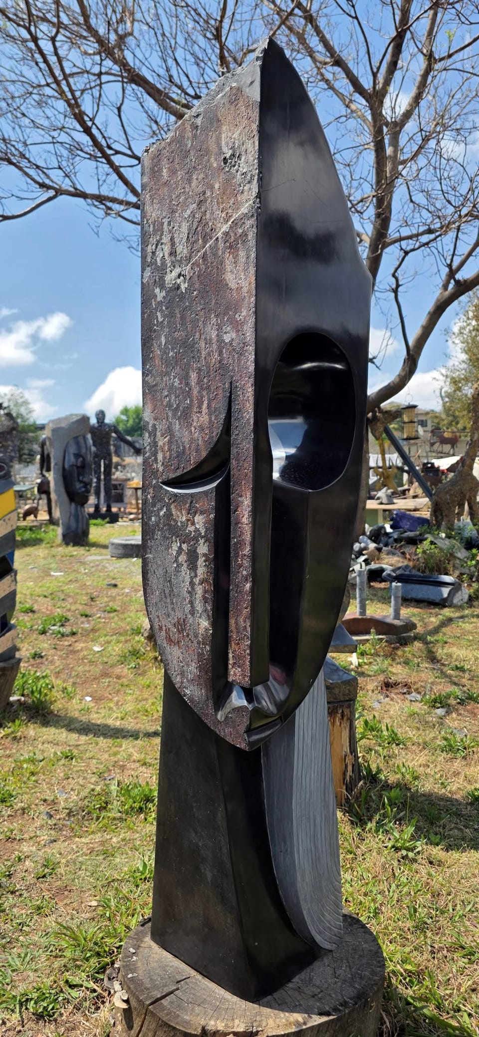 Tall stone mask whose left side keeps the rust-coloured natural rind of the block, with a polished oval eye on the right