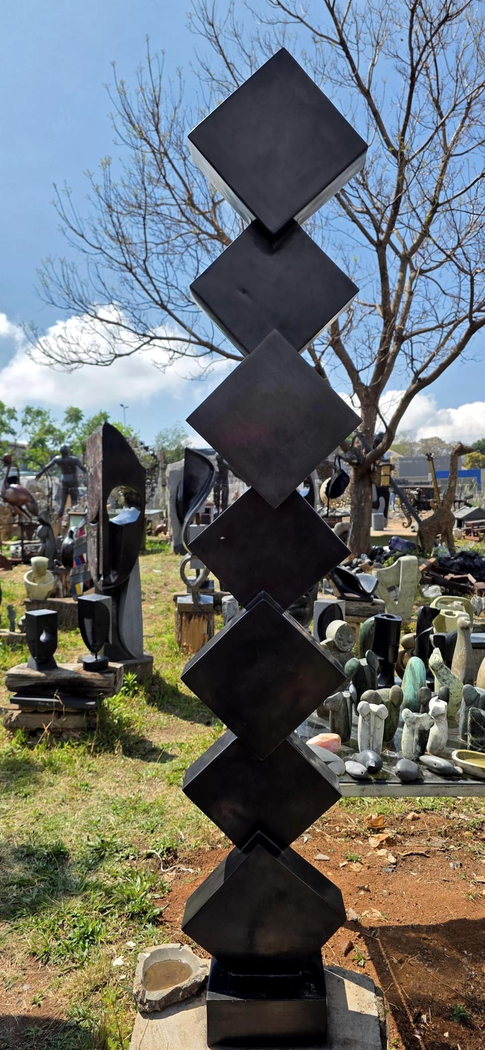 Column of dark stone cubes balanced corner to corner, standing in the workshop yard