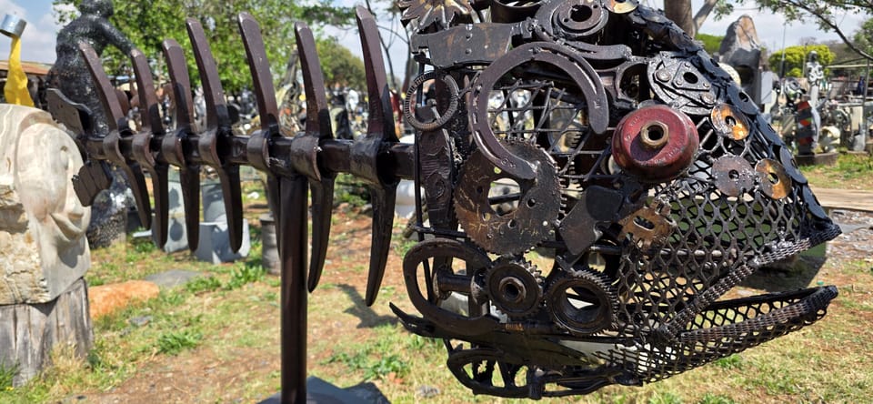 Close view of a welded metal fish built from gears and scrap parts, with a red eye