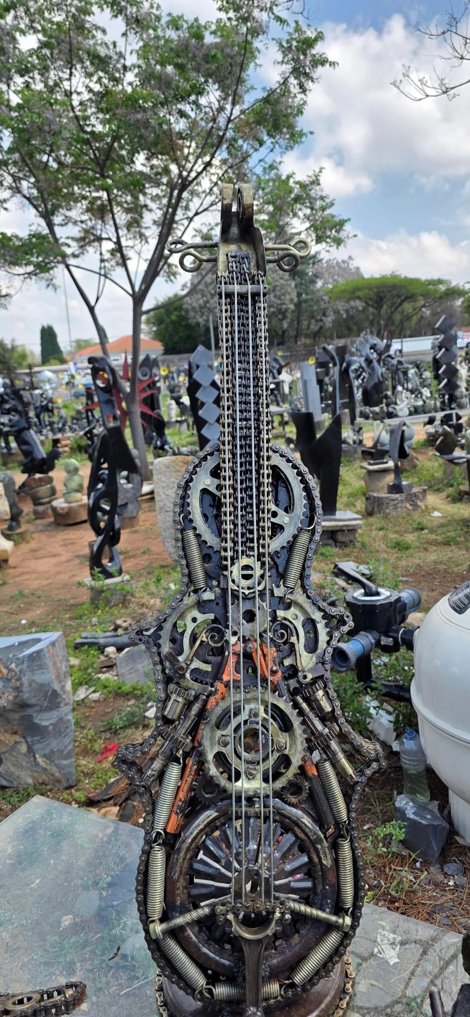 The welded metal cello seen from the front, its body built from gears, springs, chain and a clutch plate