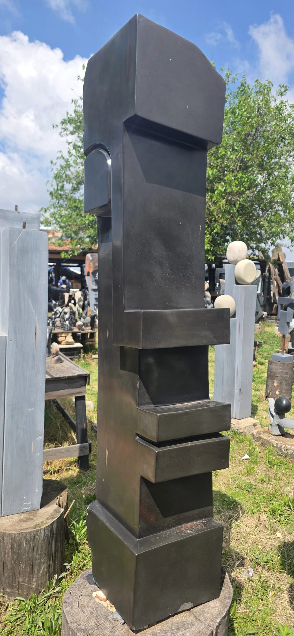 Tall dark stone column of stacked blocks with a stylised face near the top, standing outdoors