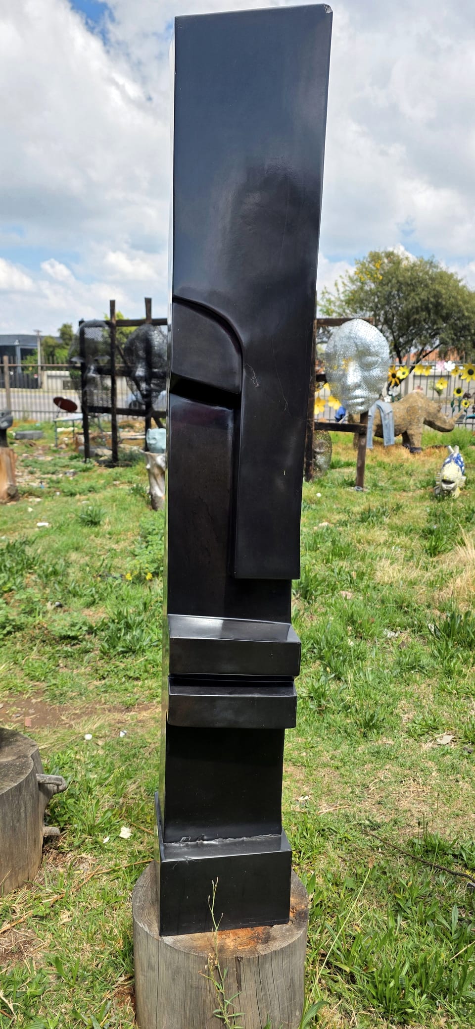 Slender dark stone column with a cut profile face, rising from a stacked base