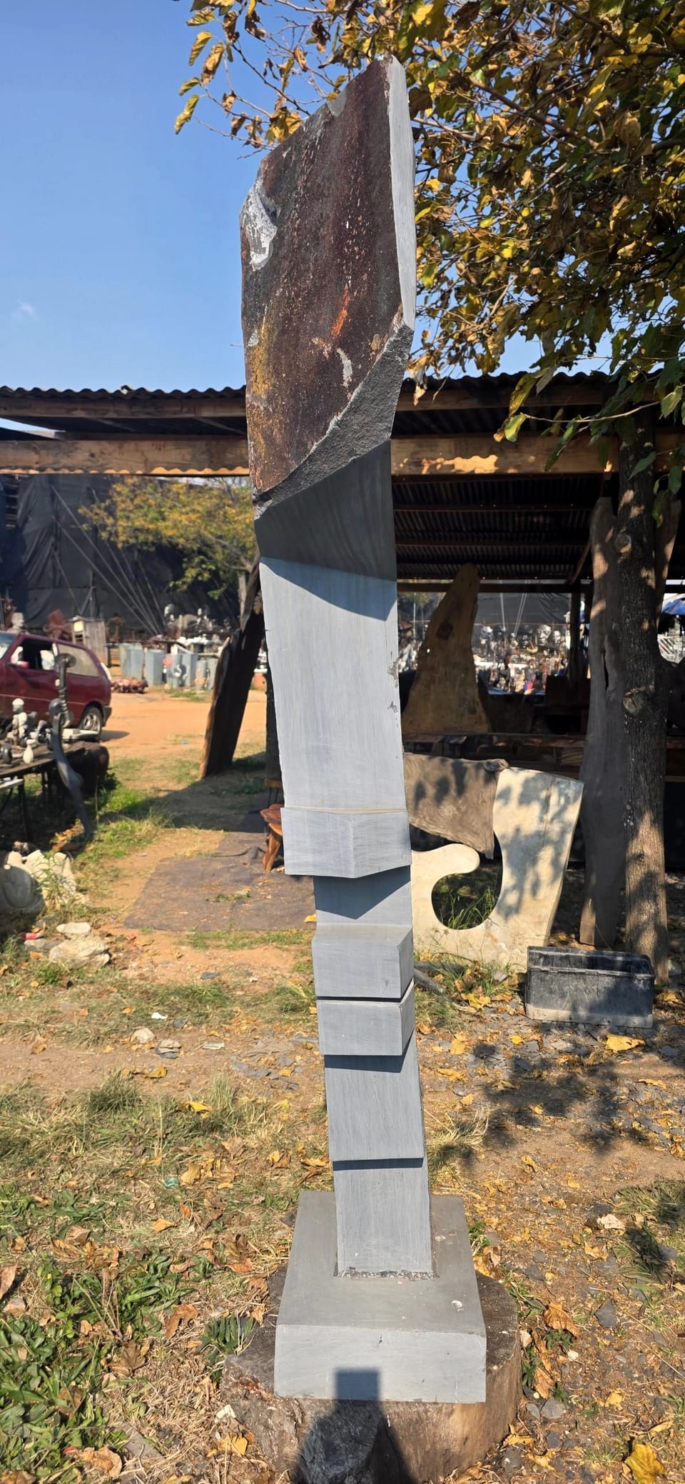 Tall slender grey stone column with stepped blocks, crowned by a slab of weathered natural rind