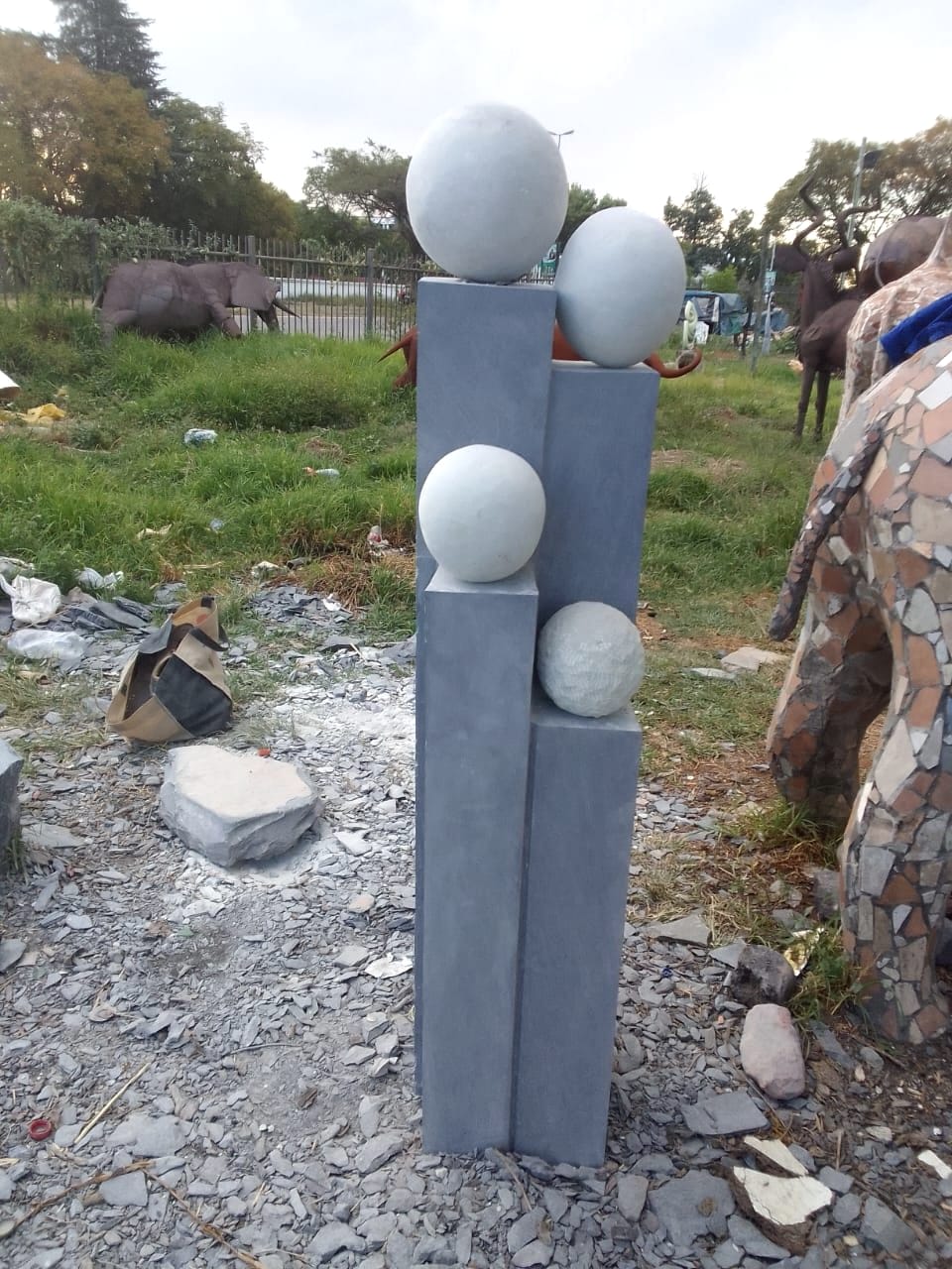 Four grey stone columns of different heights, each carrying a pale stone sphere, one sphere left rough