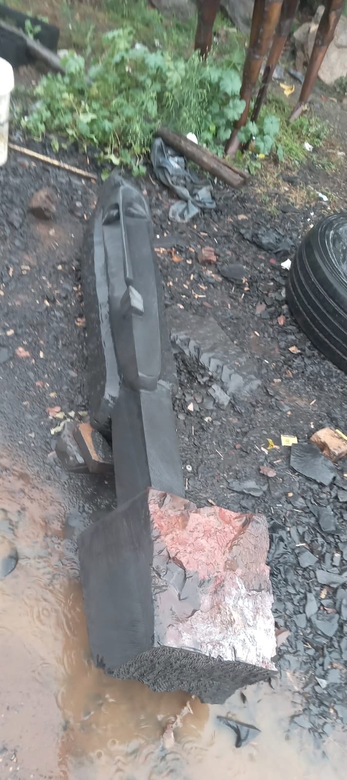 A work in progress lying in the yard: a long face carved from dark stone above an uncut block