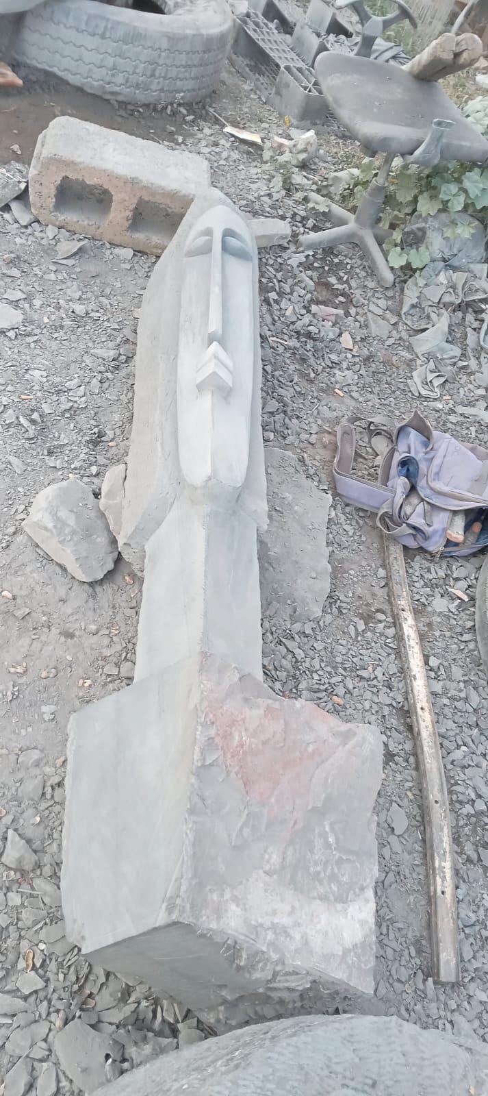 A work in progress lying among stone chips: a long face cut into grey stone, the block still rough at its base