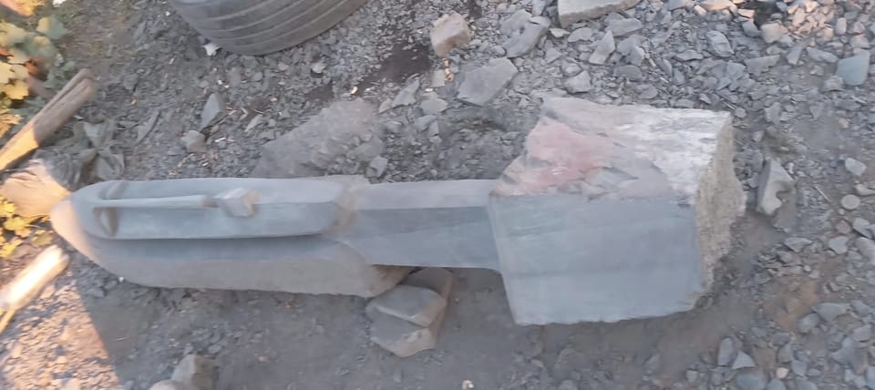 The same grey work in progress seen from the side, the long face resting on blocks above its uncut base