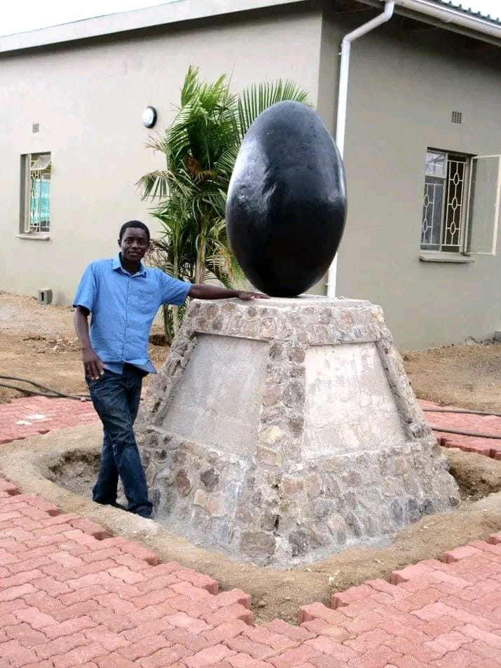 Tall dark polished egg-shaped sculpture on a stone plinth, with a man standing beside it