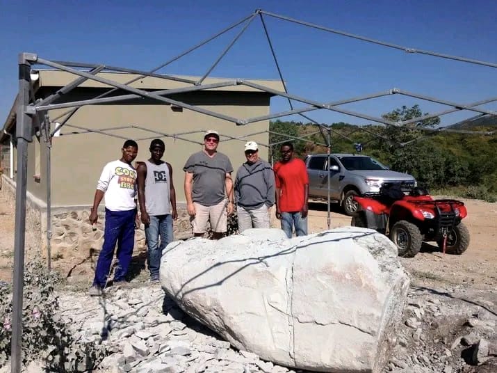 Group of men standing beside a large rough stone block in the yard