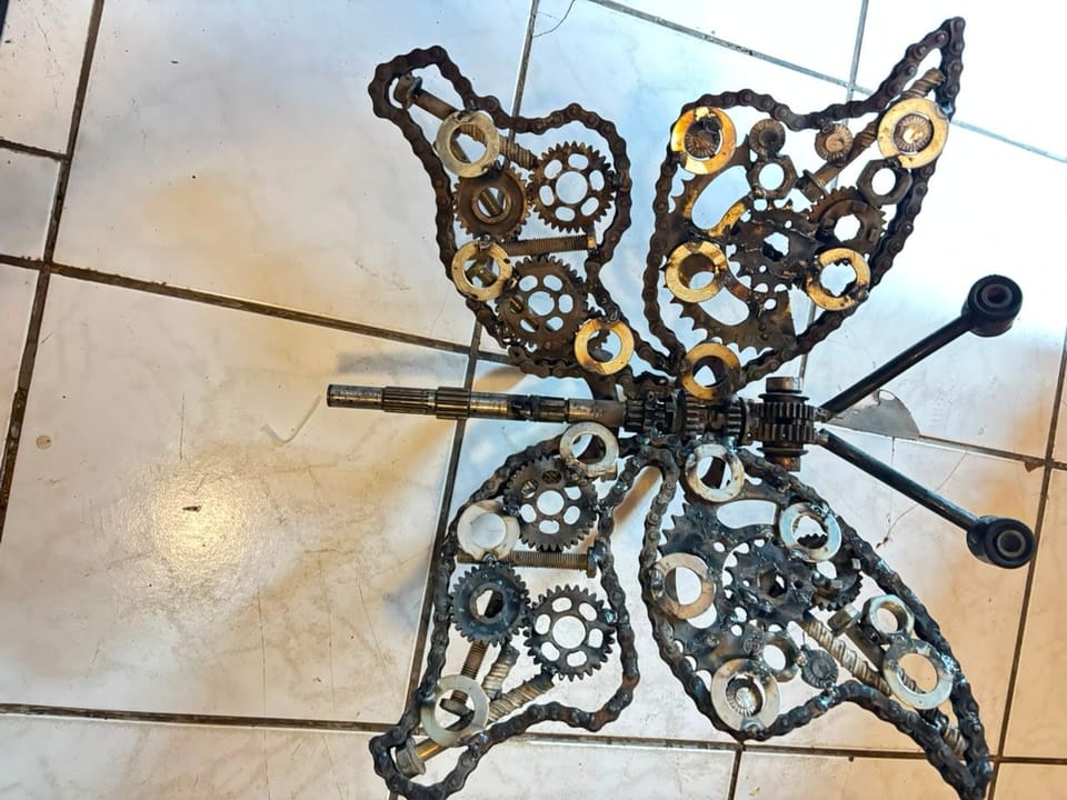 Welded metal butterfly of gears and machine parts, photographed on a tiled floor