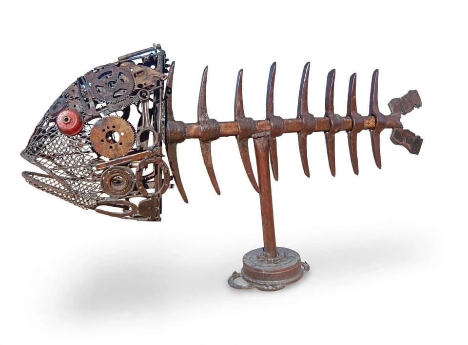 Welded metal fish skeleton with a head of gears and a red eye, on a stand, on white