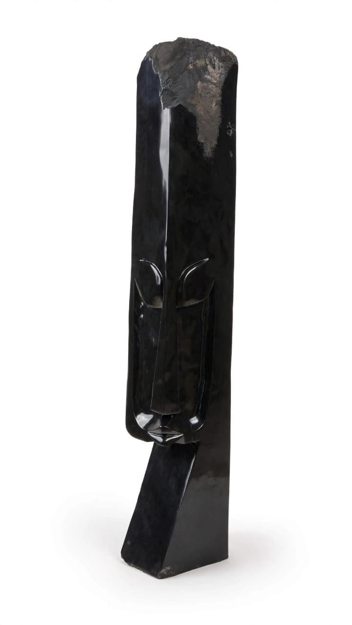 Tall slender dark stone form with a rough-cut top and a narrow carved face, on white