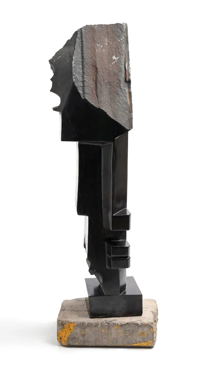 Dark polished stone face of stepped planes beneath a rough natural crown, on a stone base