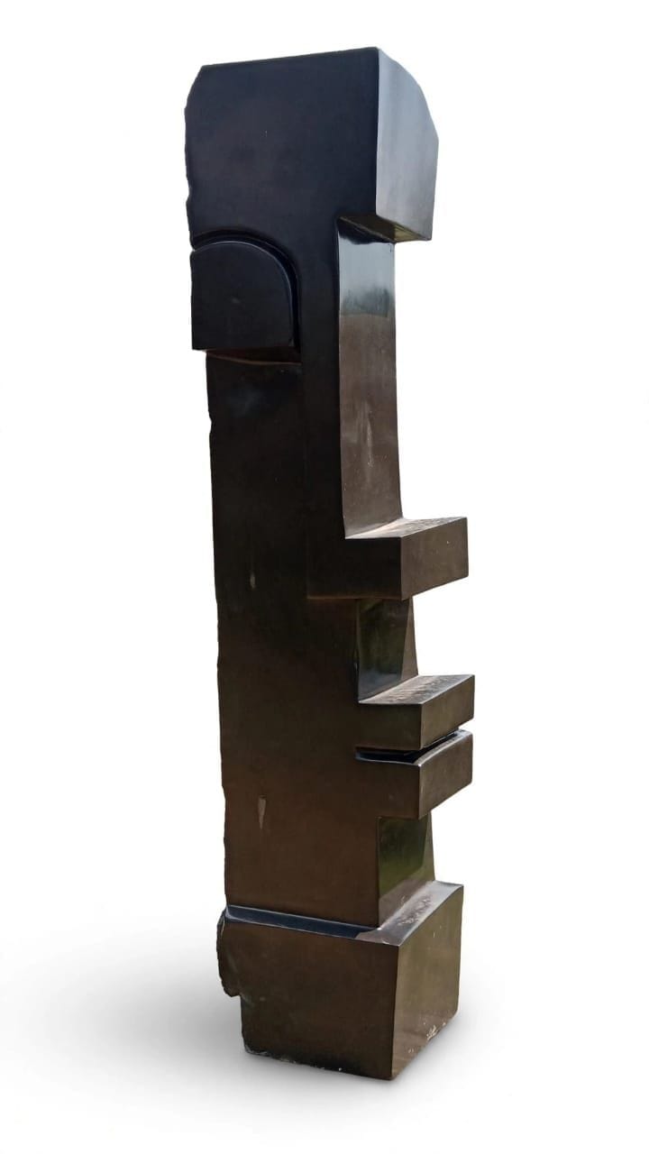 Tall dark stone column of stacked blocks with a stylised face, on white