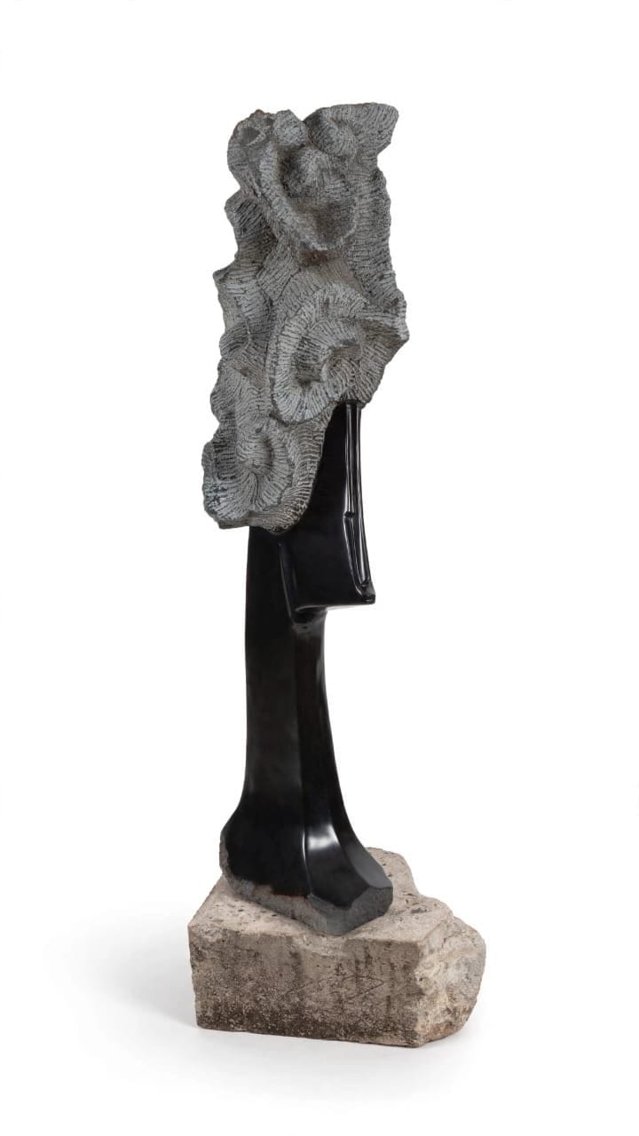 Polished dark stone face beneath a rough, textured natural crown, on a stone base, on white